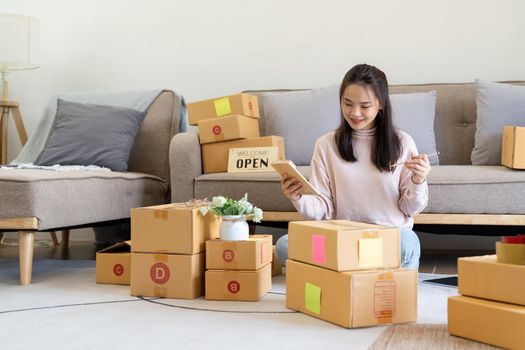 Young woman small business owner online shopping at home. confirm orders from customers preparing package product on background. SME entrepreneur or freelance life style concept.