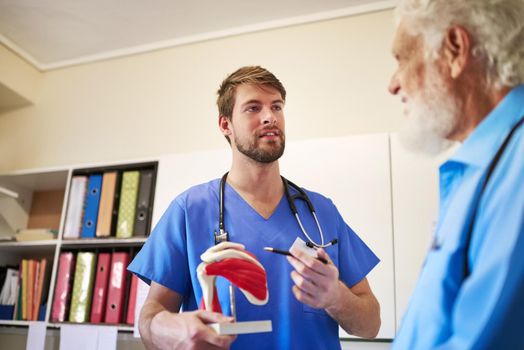 Using visuals to help him understand. a young doctor using a model to explain a diagnosis to his senior patient.