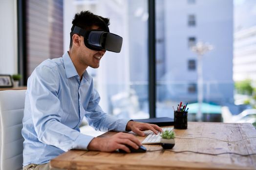 Immersed in a virtual world. a happy young businessman wearing a virtual reality headset while working at his desk in the office.
