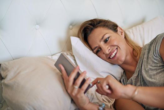 Great sleep and even greater news. an attractive woman smiling and scrolling on her cellphone in bed at home.