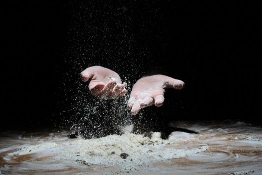 hands in flour on a black background. flour flies