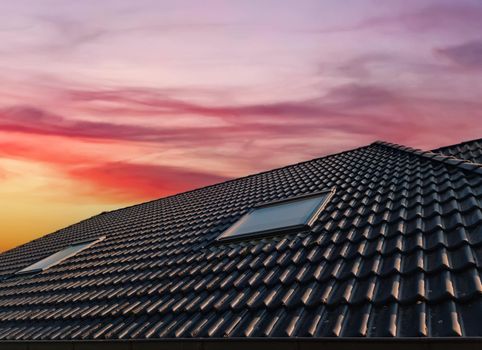 Open roof window in velux style with black roof tiles during sunset.
