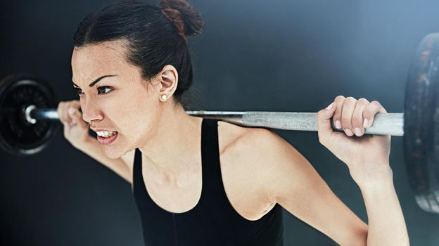 Never give up. a young woman lifting weights against a dark background.