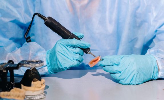 A masked and gloved dental technician works on a prosthetic tooth in his lab