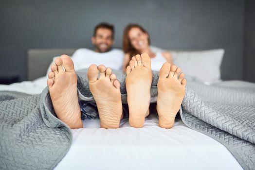 Sunday is bed day. a happy young couple relaxing in bed with their feet poking out from under the bed sheets.