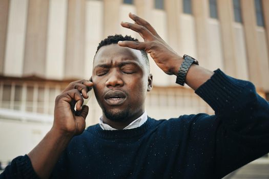 Tired, angry and stress business man talking on an annoying phone call outdoors in a city. Frustrated, pain or sick black male entrepreneur with a headache or migraine outside a urban town