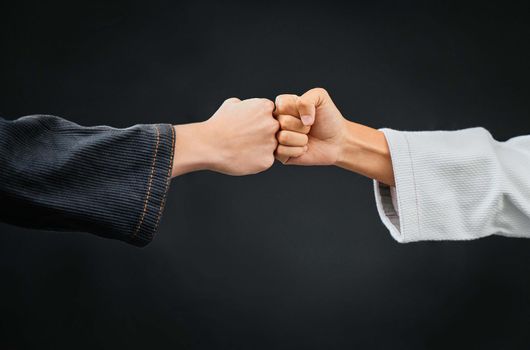 Teamwork, respect and discipline with hands fist bumping before a fight, match or mma competition. Closeup of two athletes greeting before combat sport and self defense against a black background