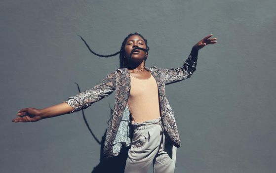 Fashion, style and trendy black woman against a gray background wall in a city, town and downtown. Street beauty model with funky, cool and hipster hair in edgy motion or movement expression outdoors
