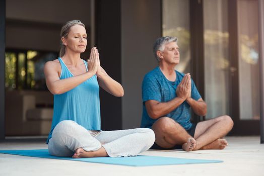 Peaceful minds are happy minds. a mature couple peacefully engaging in a yoga pose with legs crossed and hands put together.
