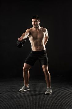 Increasing his muscle definition. Studio shot of a sporty young man working out with a kettle bell isolated on black.