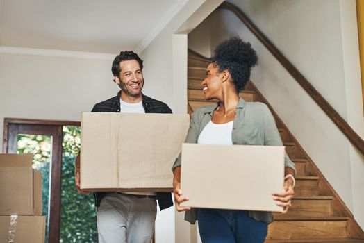 Couple homeowners moving in, carrying boxes and unpacking in new purchased home as real estate investors. Smiling, happy and cheerful interracial man and woman, first time buyers and property owners