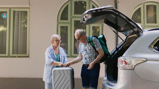 Retired couple loading voyage luggage in car trunk