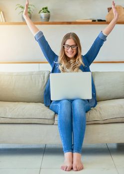 Winning with wifi. an attractive young woman raising her arms in triumph while using her laptop at home.
