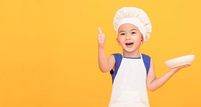 excited kid in chef uniform showing thumbs up on yellow background