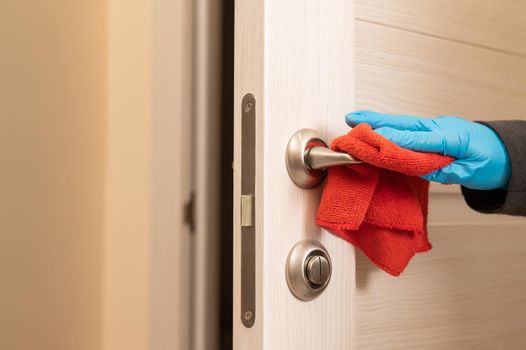 Caucasian woman in gloves wipes the door handle with a napkin.