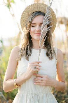 Dry branch of reed in the hands of a girl in a straw hat. Portrait