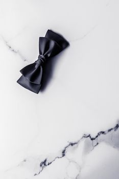 Black silk ribbon and bow on marble background, flatlay