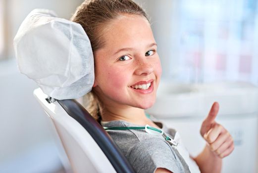 My teeth are good to go. Portrait of a young girl showing thumbs up while in the dentists chair.