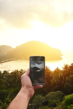 Now you can admire this view again and again. an unidentifiable tourist using a smartphone to photograph an island view.