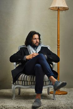 Hes a gentleman of leisure. a stylishly dressed man sitting on a chair in the studio.