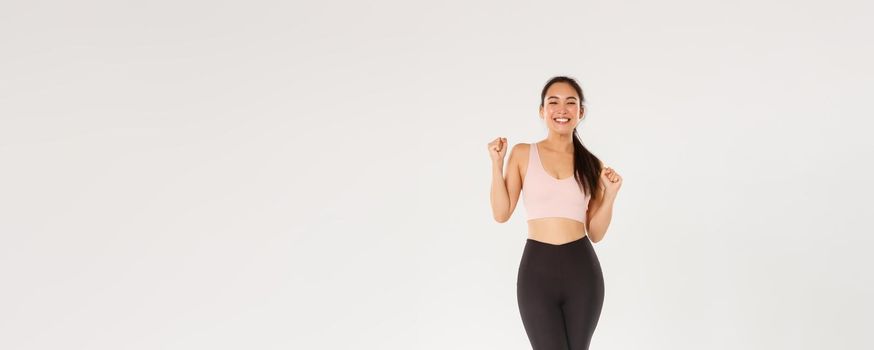 Sport, gym and healthy body concept. Full length of encouraged and motivated asian brunette girl ready for fitness training, fist pump and shouting in rejoice, gain goal with workout training app