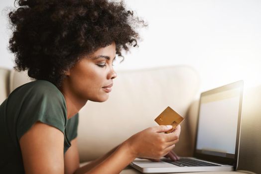 Paying the bills. a woman using her laptop on the sofa at home while holding a bankcard.