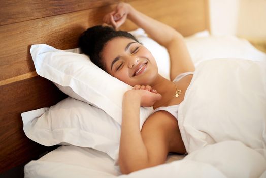 Waking up with happiness in her heart. a happy young woman waking up in bed feeling well rested.