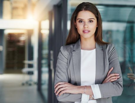You need confidence in the corporate world. Portrait of an attractive young businesswoman standing with her arms crossed in the office.