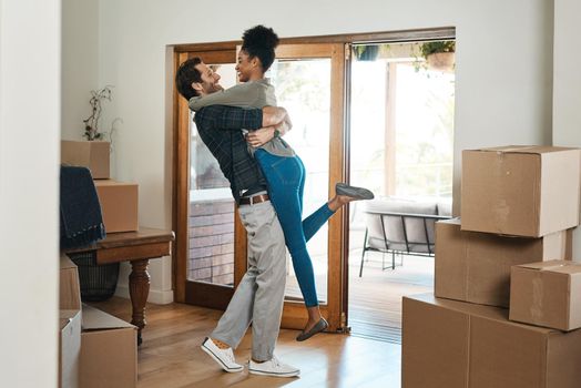 Happy couple celebrating a new home with a husband lifting his wife in excited, romantic and in love celebration together. Smiling, loving and carefree man and woman in a modern real estate property