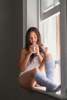 Coffee and quiet time alone. sexy young woman drinking coffee while sitting on a window ledge.