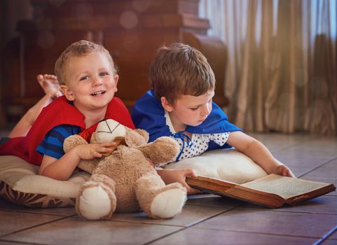 Sparking their imaginations at story time. Portrait of a happy little boy listening to his brother read a story while they lie on the floor at home.