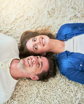 Home is wherever you are. High angle shot of an affectionate young couple lying on their living room floor.