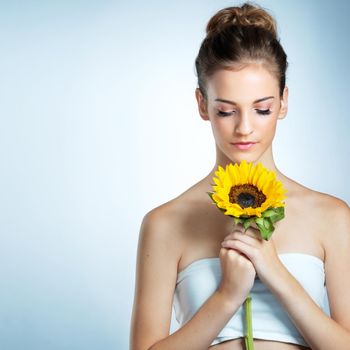 Lost in softness. Studio shot of a beautiful young woman smelling a sunflower.
