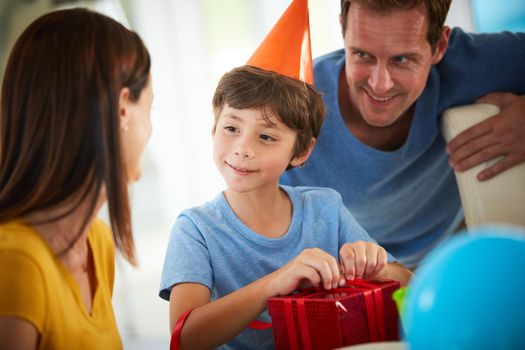 Is this one from you, Mom. a little boy opening his birthday presents surrounded by his family.