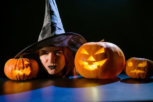 The head of an evil witch is on the table next to the glowing pumpkin jack-o-lantern