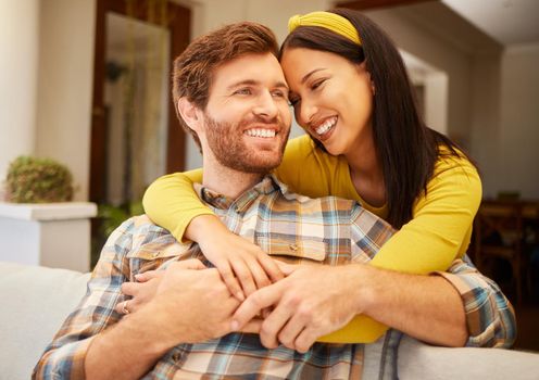 Diversity, love and happy couple in living room sofa together, sharing intimate moment at home. Freedom, smile and relax young married man embracing woman bonding on marriage anniversary
