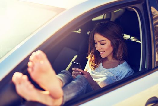 Sending a text from the road. a young woman sending a text message while sitting in her car.