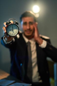 Time is an asset, use it wisely. a stressed out businessman holding a clock during a late night at work.