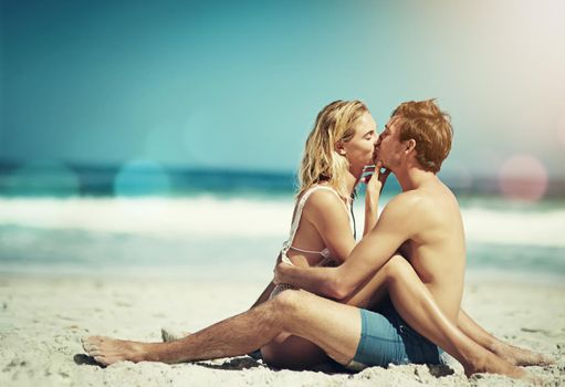 Shut up and kiss me. Full length shot of an affectionate young couple sitting face to face on the beach.
