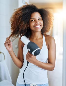 She knows how to care for curly hair. an attractive young woman drying her hair with a hairdryer at home.