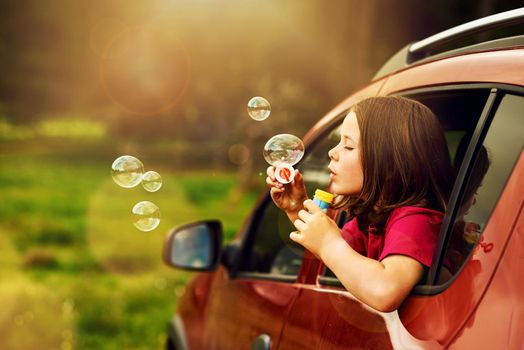 Nobodys gonna burst my bubble today. a playful little girl blowing bubbles while leaning out of a car window.