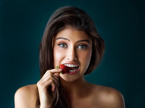 Bite into something sweet. Portrait of a gorgeous young woman biting into a strawberry against a dark background.