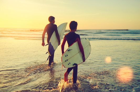 Those waves arent going to ride themselves. two young brothers carrying their surfboards while wading into the ocean.