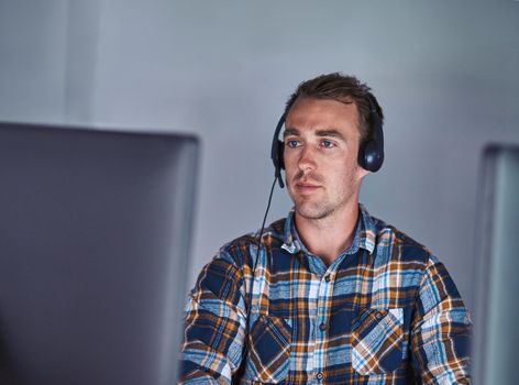 Ready and waiting for your call. a customer service agent wearing a headset while working at his computer.
