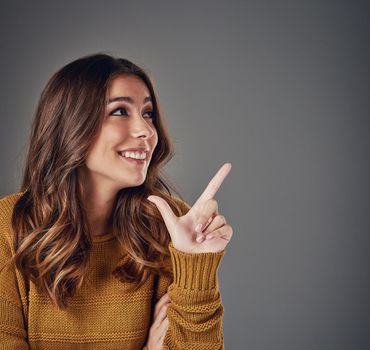 Would you look at that. an attractive young woman pointing to copyspace against a grey background.