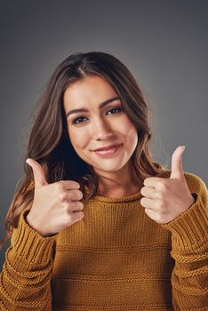 Two thumbs up for you. Portrait of an attractive young woman pulling two thumbs up against a grey background.