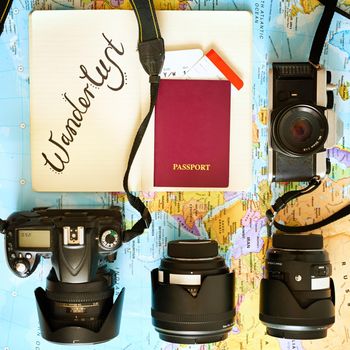 Wander all over the world. High angle shot of a map with a passport and various cameras and lenses arranged on it.