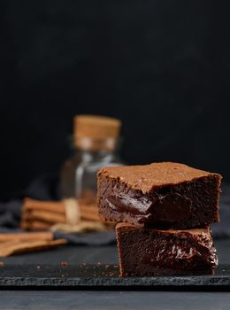 Baked pieces of chocolate brownie pie on black table, delicious dessert
