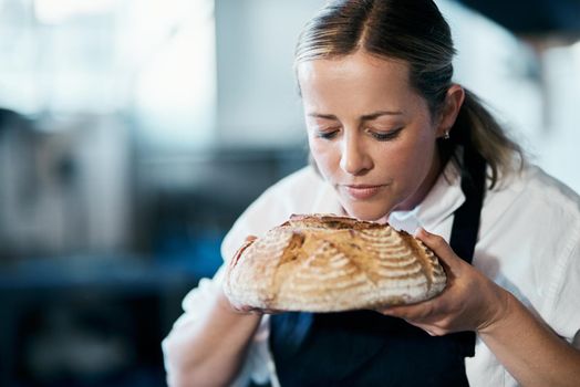 Baker, pastry chef and cafe owner smelling a loaf of fresh baked bread in the kitchen of her coffee shop. Closeup of a female cook enjoying the aroma of a freshly made dough treat or consumables