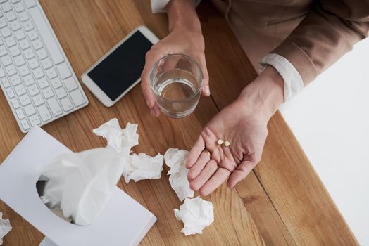 Taking medication to provide some much-needed relief. High angle shot of an unrecognisable businesswoman holding a glass of water and medication in an office.